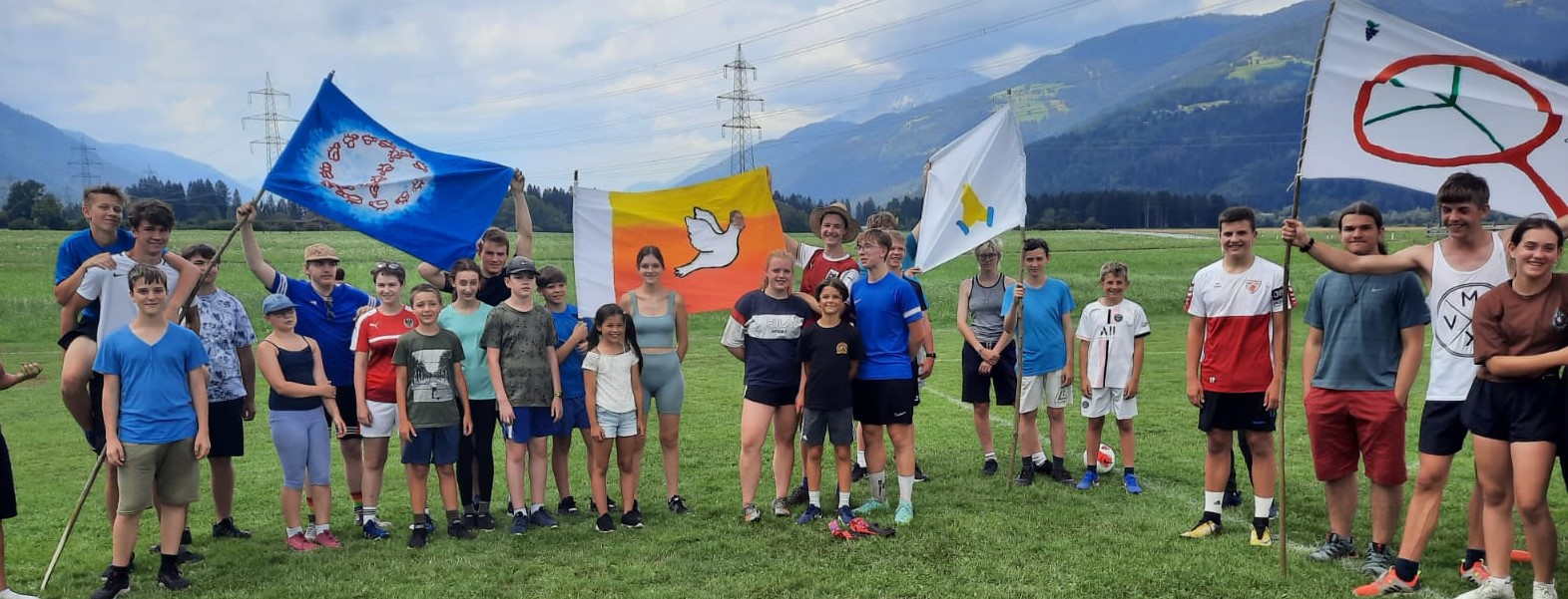 Jugendliche auf grüner Wiese mit Fahnen mit verschiedenen Friedens-Symbolen
