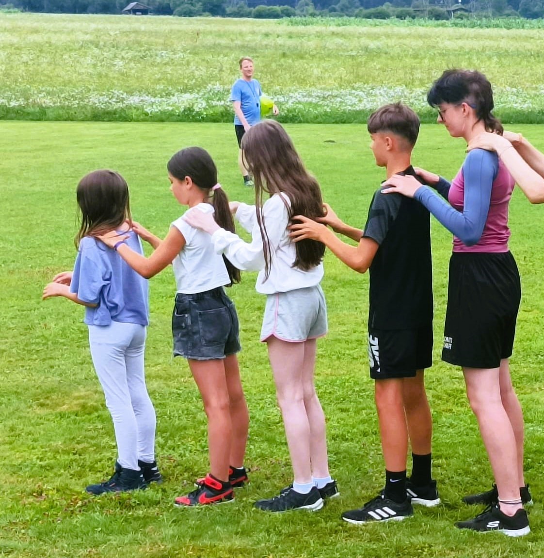 Camp 2024 - Spiel mit mehreren Jugendlichen die hintereinander stehen auf einer grünen Wiese