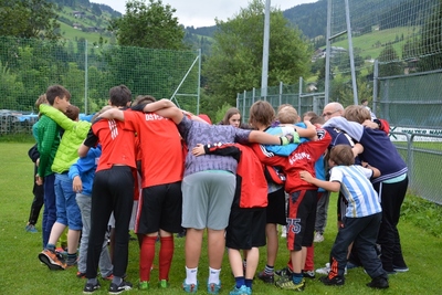 Jugendliche die auf Sportfeld im Kreis stehen mit Rücken zur Kamera.